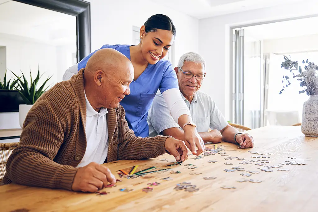 2 elderly men with a caregiver working on a puzzle as a part of a respite care program for caregiver relief. 